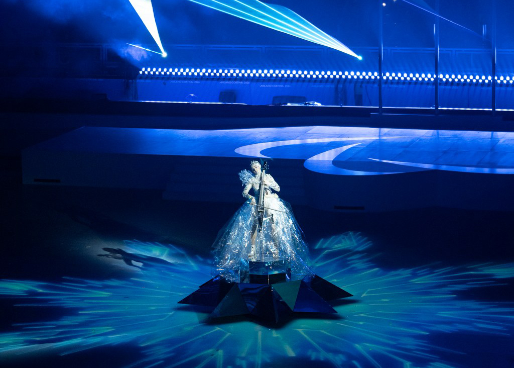 Jääkuningattareksi pukeutunut muusikko lavalla valoilla luodun lumihiutaleen keskellä.